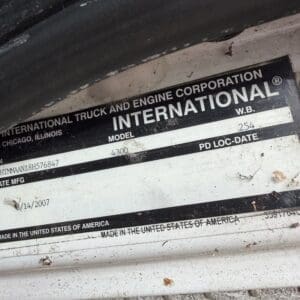 23 2 - Montana Auctions by Kevin Hill Close-up of a metal manufacturer plate on a truck showing the International brand and model information. The plate appears dirty and includes text like 'International' and model details along with 'Made in the United States of America.'