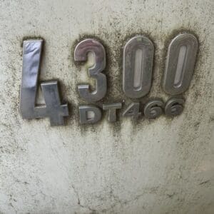 23 2 - Montana Auctions by Kevin Hill Close-up of a dirty metal badge reading '4300' and 'DT466' on a grimy surface.