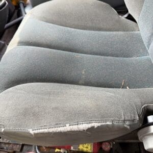 23 3 - Montana Auctions by Kevin Hill Tabricked car seat with a large tear along the bottom front edge, exposing foam and frayed fabric, dusty interior floor with hoses and rust nearby.