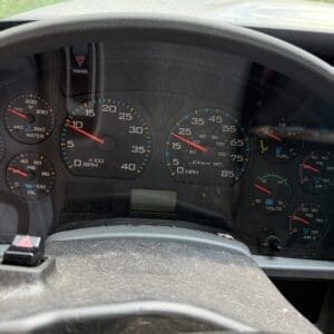 23 4 - Montana Auctions by Kevin Hill Dashboard view of a dusty car interior with a gauge cluster: tachometer, speedometer, fuel and oil gauges, seen through the steering wheel. Outside shows greenery.