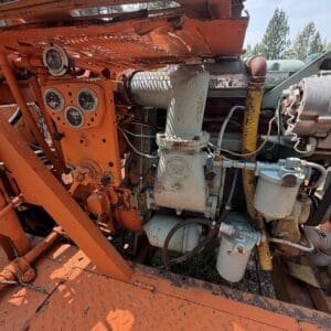 25 3 - Montana Auctions by Kevin Hill Close-up of orange industrial engine with gauge panel and rusty pipes on a metal platform outdoors.