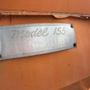 25 4 - Montana Auctions by Kevin Hill Close-up of a silver nameplate on an orange, rusted surface reading 'Model 155' read from left to right.