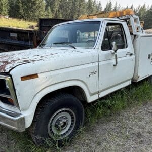 27 1 - Montana Auctions by Kevin Hill Old white utility truck with rusted hood in a grassy, rural area and a toolbox bed on the back.