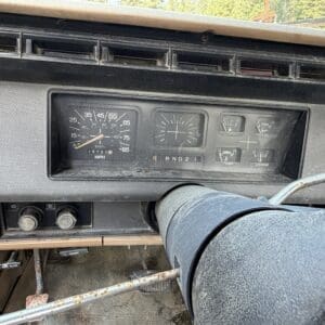 27 3 - Montana Auctions by Kevin Hill Vintage car dashboard with central speedometer and gauges, weathered steering column in foreground, and basic controls below.