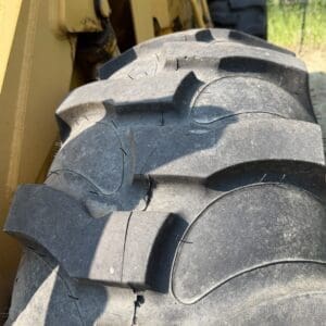 3 2 - Montana Auctions by Kevin Hill Close-up of a cracked, oversized tire on a yellow construction vehicle outside.