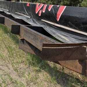 31 1 - Montana Auctions by Kevin Hill Row of rusted steel beams supporting a black plastic construction barrier along a grassy field on a sunny day