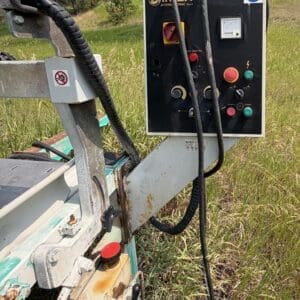 32 3 - Montana Auctions by Kevin Hill Control panel mounted on a rusted outdoor machine in a grassy field, with red and green buttons and cables connected to the unit.