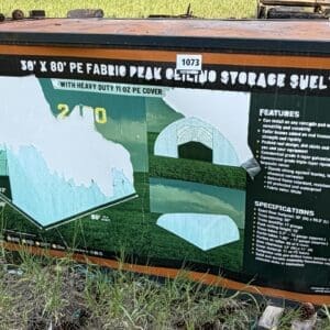 35 1 - Montana Auctions by Kevin Hill Orange storage shelter with an informational graphic about a 38' x 80' fabric peak shelter, showing diagrams and specs on a metal panel.