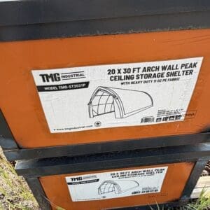 35 5 - Montana Auctions by Kevin Hill Orange storage shelter packaging with label that reads '20 x 30 ft arch wall peak ceiling storage shelter' and a diagram of the tent structure (TMG Industrial).