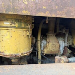 4 10 - Montana Auctions by Kevin Hill Rusty yellow industrial engine bay with a large cylindrical filter housing and exposed hoses and rusted metal surfaces
