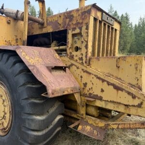 4 11 - Montana Auctions by Kevin Hill Rusty yellow heavy equipment with a large treaded tire, left side visible, sits in a grassy field.