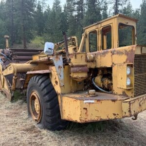 4 2 - Montana Auctions by Kevin Hill Old yellow, rusted heavy equipment with a Michigan-branded grille, parked on a dry grassy area with trees in the background.