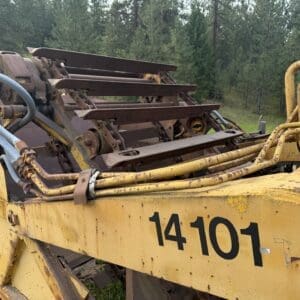 4 5 - Montana Auctions by Kevin Hill Old yellow industrial equipment with rust and exposed hydraulic lines, number 14101, in a grassy outdoor area with trees in the background.