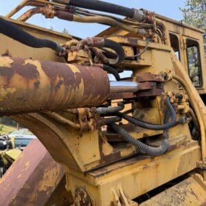 4 8 - Montana Auctions by Kevin Hill Close-up of a yellow, rusted hydraulic arm with interconnected hoses on heavy machinery outdoors.