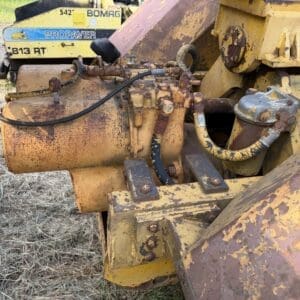 4 9 - Montana Auctions by Kevin Hill Close-up of rusted hydraulic hoses and cylinders on a yellow construction machine outdoors in a field.