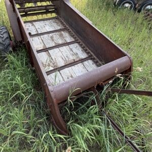 43 3 - Montana Auctions by Kevin Hill Rusty metal farm wagon with wooden slats, overgrown by tall grass in a field, with a trailer in the background