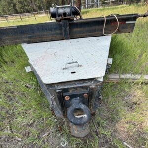 45 4 - Montana Auctions by Kevin Hill A rusted trailer hitch and mounting assembly with a circular tow ring, chains, and a diamond-plate access panel in a grassy outdoor setting.