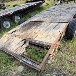 46 2 - Montana Auctions by Kevin Hill Old, weathered flatbed trailer with a split wooden deck and rusted metal frame, sitting in tall grass.