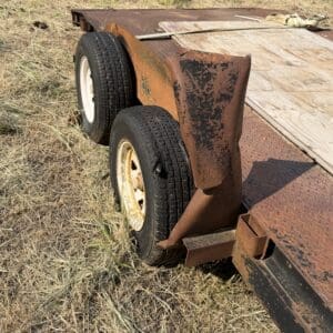 48 1 - Montana Auctions by Kevin Hill Rusty utility trailer with two wheels and a wooden deck resting on dry grass in an open field.