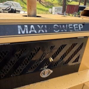 5 2 - Montana Auctions by Kevin Hill Close-up of a MAXI-SWEEP industrial sweeper with a black vent panel and yellow body outdoors.