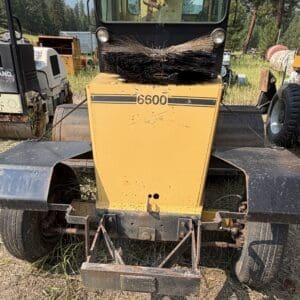 5 3 - Montana Auctions by Kevin Hill Front view of a yellow road sweeper with a large circular brush on the hood, model 6500, parked in a grassy lot.