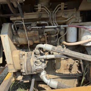 5 4 - Montana Auctions by Kevin Hill Close-up of a dusty diesel engine with hoses and a hydraulic pump in an industrial machine.