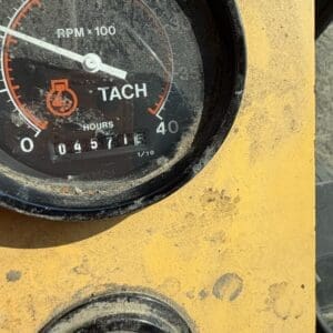 5 6 - Montana Auctions by Kevin Hill Close-up of a dusty tachometer on a yellow control panel, showing RPM x100 and an hour counter reading a few hours.