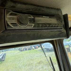 5 9 - Montana Auctions by Kevin Hill Dusty Pioneer car stereo head unit mounted in a vehicle, with the windshield and yard equipment visible outside the cabin.