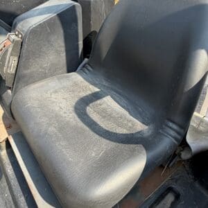 6 3 - Montana Auctions by Kevin Hill Seat inside a dusty construction vehicle cabin, showing a worn black ergonomic chair with nearby levers and controls.