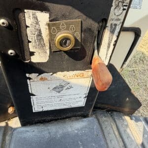 6 4 - Montana Auctions by Kevin Hill Industrial machine control panel with a brass lock and orange safety lever, warning labels visible below the lock area on a dusty black surface contextualizing caution instructions.