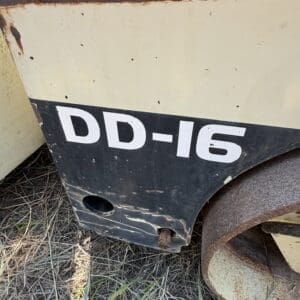 6 6 - Montana Auctions by Kevin Hill Close-up of a weathered industrial machine panel with beige and black paint, rust along the edges, and the partial label 'DD-16' visible on the lower portion.