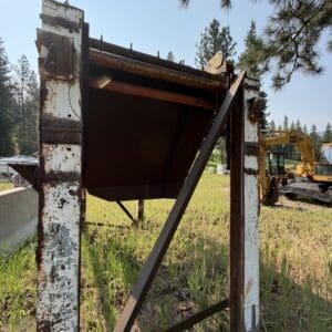 7 2 - Montana Auctions by Kevin Hill Rusty metal framework in a grassy field with a yellow CAT excavator visible in the background.