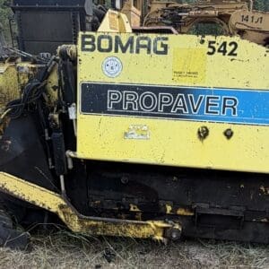 8 2 - Montana Auctions by Kevin Hill Yellow BOMAG Propaver asphalt paver with a blue stripe, model numbers 542 and 813 RT visible, parked on grass.