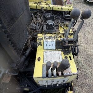 8 3 - Montana Auctions by Kevin Hill Yellow control console on a weathered piece of heavy machinery, featuring multiple black levers and worn labels outdoors in a dusty yard.