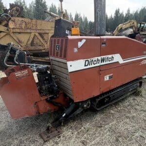 9 1 - Montana Auctions by Kevin Hill Red Ditch Witch trenching machine with tracks, parked on dirt near rusted heavy equipment. Brand name visible on side: Ditch Witch (T1700).