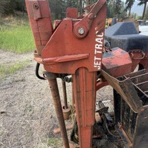 9 2 - Montana Auctions by Kevin Hill Close-up of a red, rusty hydraulic attachment on a farm implement in a grassy, wooded field with trees in the background.