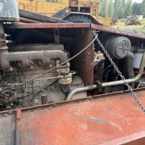 9 4 - Montana Auctions by Kevin Hill Rusty diesel engine mounted on a red maintenance platform, with hoses, chains, and heavy equipment in a scrapyard.