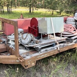 IMG_8524 - Montana Auctions by Kevin Hill Rusty flatbed trailer with tools, hoses, tires, and metal equipment in a grassy field with trees in the background