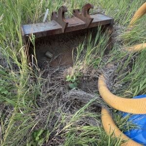 IMG_8530 - Montana Auctions by Kevin Hill Rusty metal irrigation valve box partially buried in tall grass, with yellow hoses nearby.