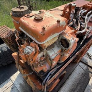 IMG_8535 - Montana Auctions by Kevin Hill Rusted orange industrial engine with peeling paint and a large tire nearby on a wooden deck outdoors.