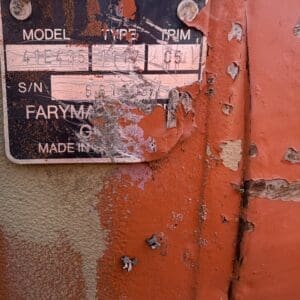 IMG_8536 - Montana Auctions by Kevin Hill Close-up of a rusted machinery label on orange paint, showing faded 'MODEL', 'TYPE', 'S/N' with numbers barely legible after peeling paint.