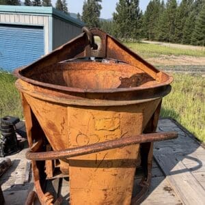 IMG_8538 - Montana Auctions by Kevin Hill Rusty orange portable concrete mixer on a trailer in a grassy yard with pine trees in the background.