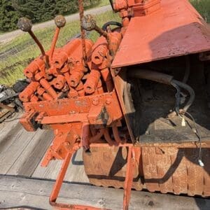 IMG_8541 - Montana Auctions by Kevin Hill Close-up of rusty orange hydraulic controls on a flatbed trailer, outdoors by grass and trees in the background.