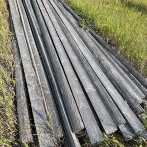IMG_8545 - Montana Auctions by Kevin Hill Pile of weathered wooden planks stacked in a grassy field by the roadside, ready for use or disposal.