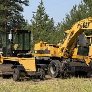 IMG_8556 - Montana Auctions by Kevin Hill Group of construction machines in a field: a yellow excavator, a compactor, and a wheeled roller with trees in the background.
