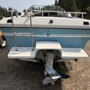 IMG_8705 - Montana Auctions by Kevin Hill Rear view of a blue-and-white speedboat on a trailer, showing the stern, stainless railings, and an attached outboard motor tucked under the stern