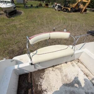 IMG_8730 - Montana Auctions by Kevin Hill View of a boat deck with a white and red padded bench, dry dirt and pine needles, outdoors in a grassy field with heavy machinery in the background