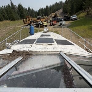 IMG_8736 - Montana Auctions by Kevin Hill View from the bow of a boat toward a dirt road with heavy construction equipment and trucks in a forested area.