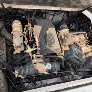 IMG_8737 - Montana Auctions by Kevin Hill Dusty boat engine with a MerCruiser cover and tangled hoses and wiring in a cramped engine bay.