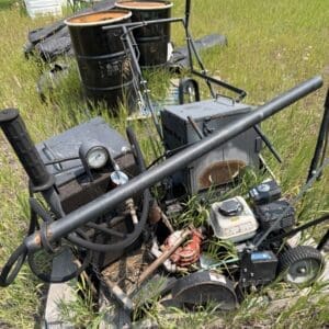IMG_8840 - Montana Auctions by Kevin Hill Old portable pump/compressor unit with a pressure gauge, hoses, and a small engine, abandoned in tall grass outdoors.